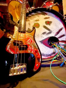 photo of a bass guitar leaning against a bass drum. The drumhead has a vomiting face painted onto it.